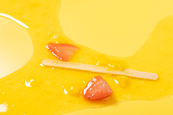 angle view melted mango fruit flavor with strawberry slices popsicle on yellow background - Photo, Image
