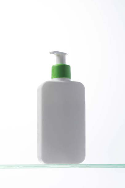 A mockup of a white dispenser with a cosmetic product for skin care of the face and body on a glass shelf. Shower gel, facial cleanser. - Photo, image