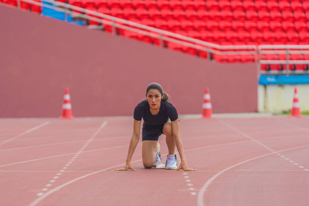 Atleta asiática en el bloque de inicio, lista para su práctica de carrera de velocidad en la pista del estadio, personificando la preparación - Foto, imagen