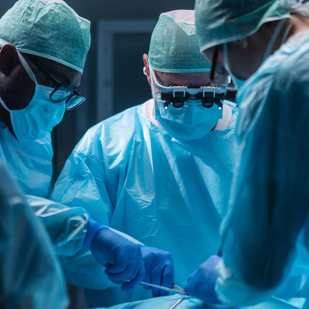 Ein vielseitiges Team professioneller Ärzte führt einen chirurgischen Eingriff in einem modernen Operationssaal mit High-Tech-Geräten und -Technologie durch. Chirurgen arbeiten daran, den Patienten im Krankenhaus zu retten - Foto, Bild
