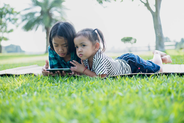 Southeast Asian girls play mobile phones outdoors in the courtyard during the summer on vacation. - Фото, зображення