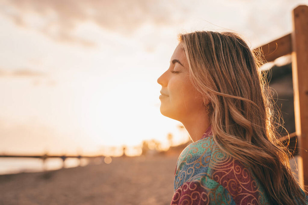 Portrét jedné mladé ženy na pláži se zavřenýma očima, užívající si volného času a svobody venku. Bavit se odpočinkem a prožívat šťastné chvíle. - Fotografie, Obrázek