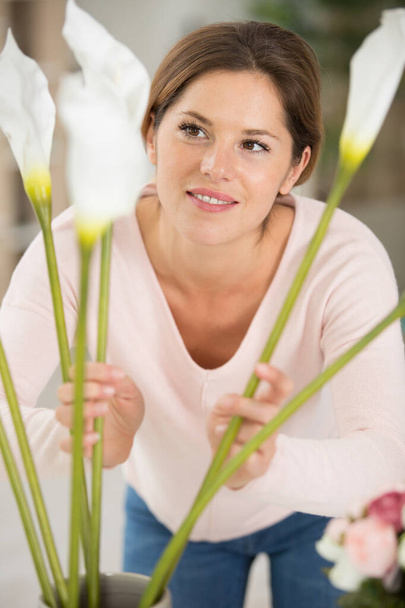 beautiful brunette woman arranging calla lilies in a vase - Fotó, kép