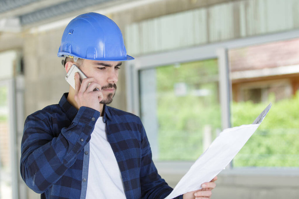 young architect wearing protective helmet speaking on telephone - Photo, image