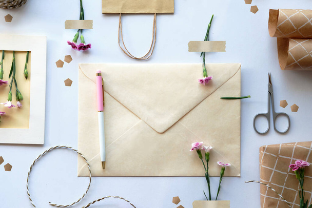Envelope and self made greeting card concept with fresh carnation flowers, knolling style. Wrapped gift, paper postcard, paper envelope, cord, scissors and purple carnations. - Foto, immagini