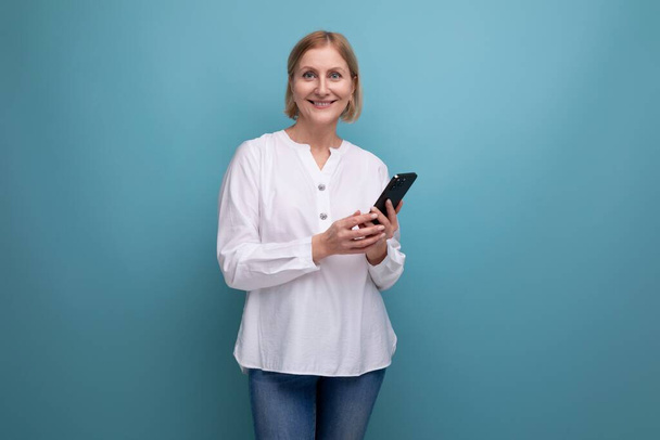 zdravý štíhlý blond zralý žena s smartphone chatování na pozadí studia. - Fotografie, Obrázek
