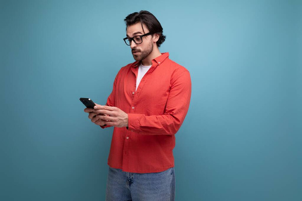 cute caucasian brunette 30s man in a red shirt communicates online in the phone. - Photo, Image