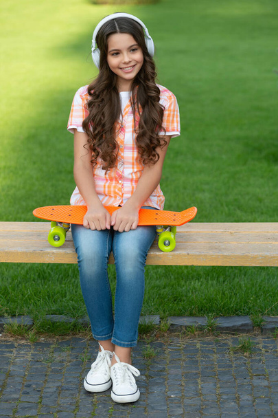 cheerful teen girl with skateboard in headphones. teen girl with skateboard outside. teen girl with skateboard listen music. teen girl with skateboard outdoor. - Foto, Imagen