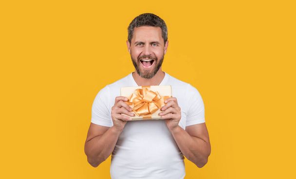 man hold gift box isolated on yellow background. man hold gift box in studio. man with gift box for holiday. man holding occasion gift box. - Foto, imagen