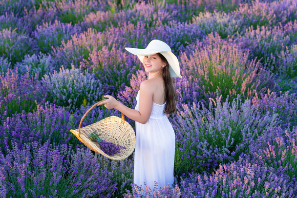 smiling teen girl with lavender in field. Teen girl with lavender flower standing in the field. teen girl with lavender holding a flower bouquet. Teen girl in a dress walking in lavender park. - Fotoğraf, Görsel