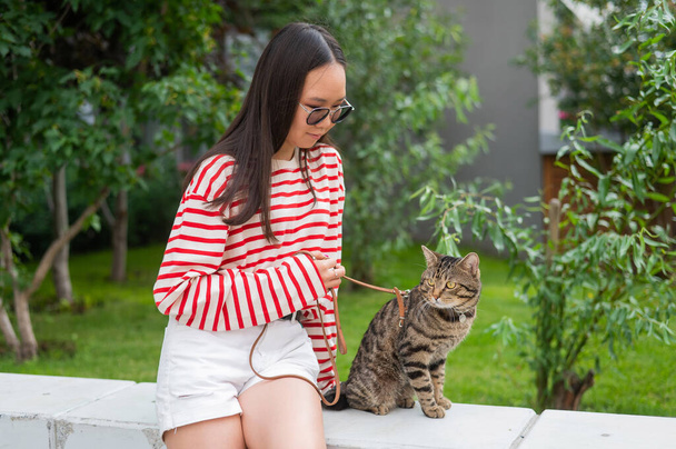 Young woman and tabby cat sitting on a bench outdoors - Foto, Imagem