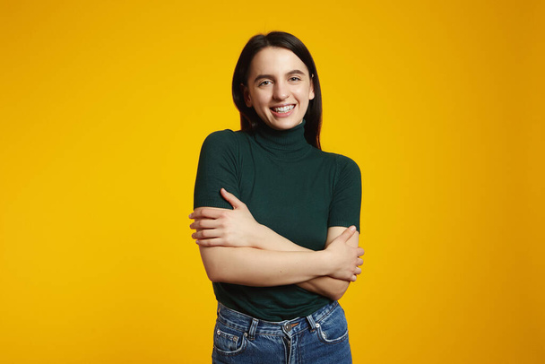 Pleased satisfied caucasian girl hugging herself and smiling, feeling comfortable and fulfilled, isolated over yellow background - Photo, Image
