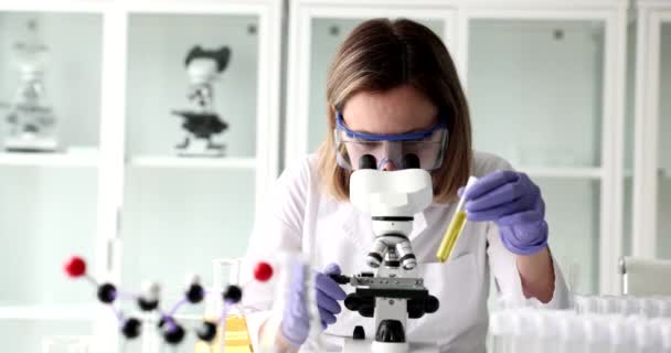 Chimiste regarde microscope tient éprouvette avec liquide jaune biologique. Contrôle de qualité de l'huile et des produits pétroliers - Séquence, vidéo