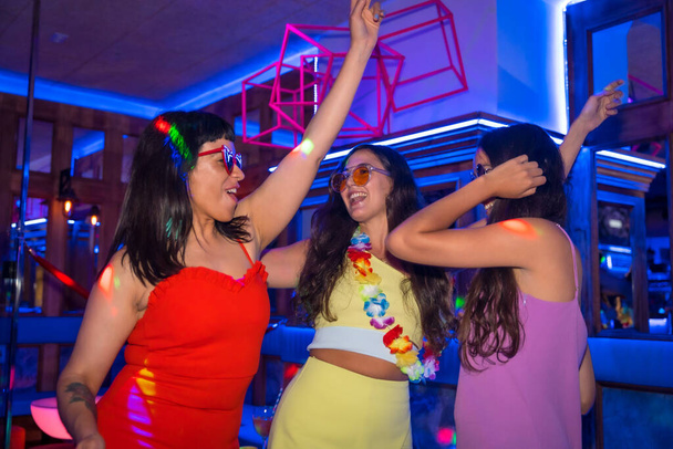 Female friends in a disco dancing smiling at a night party on summer vacation in a pub - Foto, Imagen