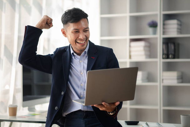 Man holding laptop and celebrating, he is young energetic businessman, modern business management, start-up company run by young people, modern entrepreneur with fresh ideas. to be a business leader. - Photo, Image