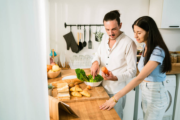 Egy kaukázusi boldog pár áll a konyhában, sok zöldséget és gyümölcsöt készítve a közös főzéshez. Egy pár szeret egészséges összetevőkkel főzni. Egészséges wellness életmód koncepció. - Fotó, kép