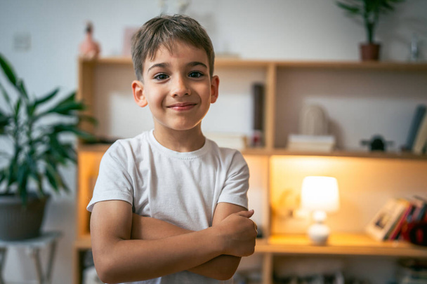 Bir çocuk, mutlu bir beyaz anaokulu portresi. Evdeki fotokopi odasında duruyor. Beyaz tişört giyip kameraya bakıyor. - Fotoğraf, Görsel