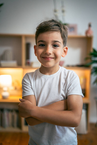 Bir çocuk, mutlu bir beyaz anaokulu portresi. Evdeki fotokopi odasında duruyor. Beyaz tişört giyip kameraya bakıyor. - Fotoğraf, Görsel