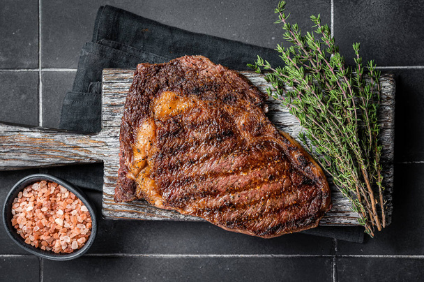 Barbecue aged wagyu Rib Eye beef meat steak with thyme on wooden board. Black background. Top view. - Foto, Bild