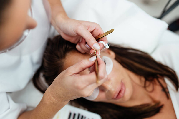 Beautiful young adult woman receiving professional eyelash makeup treatment. Cosmetician is smiling and looking at camera. Beauty and cosmetics business.  - Fotografie, Obrázek