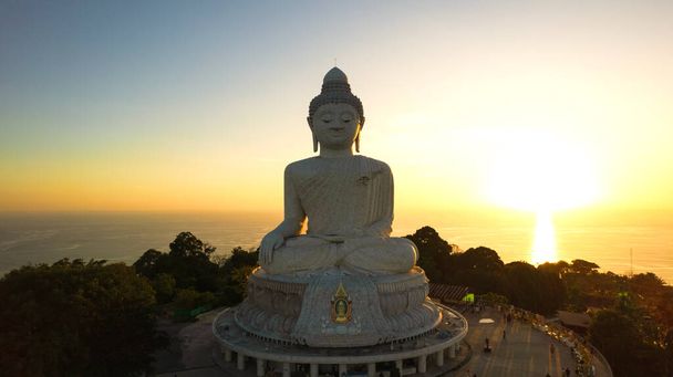 Великий Будда на заході сонця з дрона. Фантазія. Люди піднімаються сходами до статуї. Зелені пагорби острова навколо. Вдалечині яскраве сонце сідає над морем. Вид згори - Фото, зображення