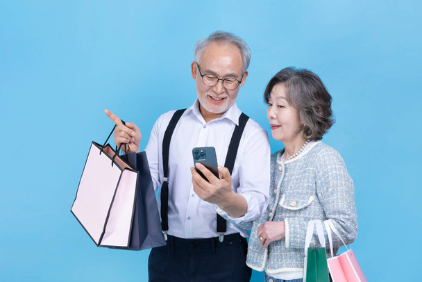 active young senior Korean Asian couple holding shopping bags and smartphone - Photo, image