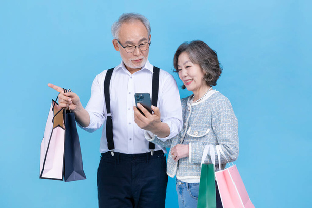 active young senior Korean Asian couple holding shopping bags and smartphone - Фото, изображение