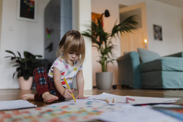 Cute little girl drawing with crayons, sitting on the floor in the living room. - Φωτογραφία, εικόνα