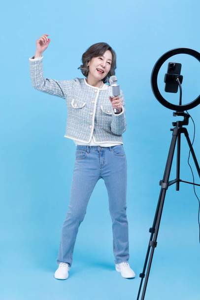 singing active young senior Korean Asian woman with smartphone, mobile karaoke concept - Фото, изображение