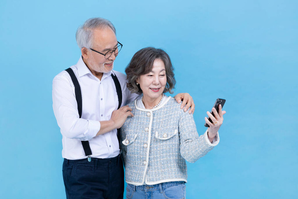 active young senior Korean Asian couple looking at smartphone - Foto, imagen