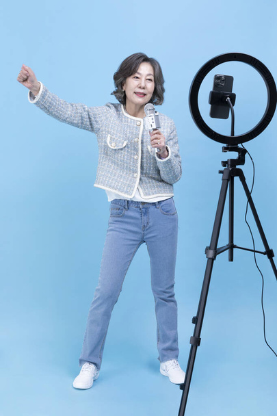 singing active young senior Korean Asian woman with smartphone, mobile karaoke concept - 写真・画像