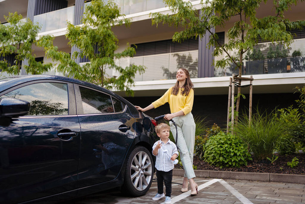 Smiling mother and her little son charging their electric car on the street. Cute boy holding model of wind turbine. - Foto, Imagem