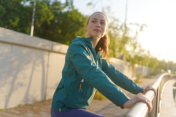 Young female runner enjoying sunrise before her early morning run. Waist up portrait of fitness girl in sportswear preparing for evening exercise. Outdoor workout concept. - Фото, зображення