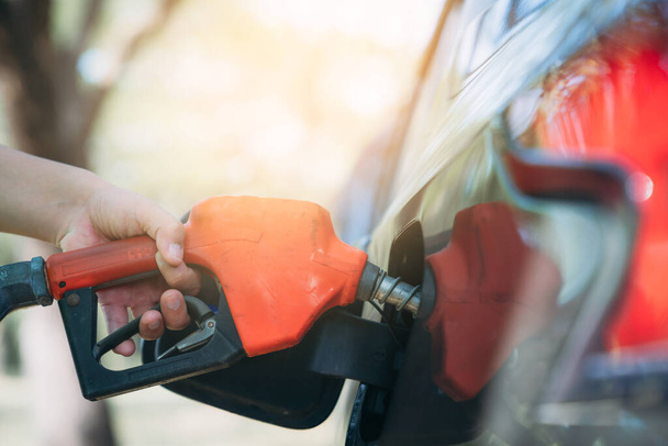 Closeup hand refueling the car at a gas station. Refill gasoline fuel in car. A man holding orange gas pump. - Фото, изображение