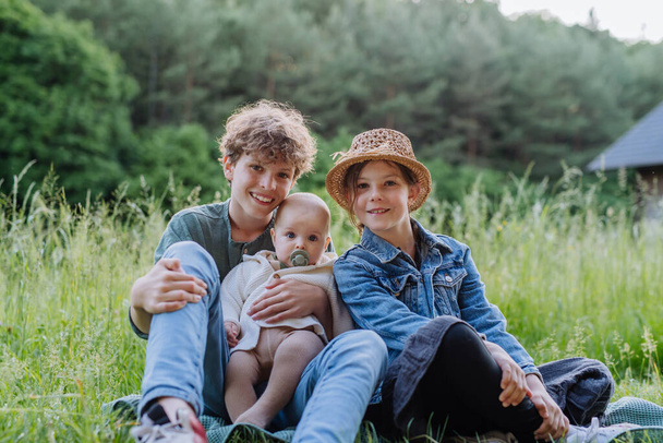 Portrait of three children, siblings sitting in a grass, having fun together. - Foto, afbeelding