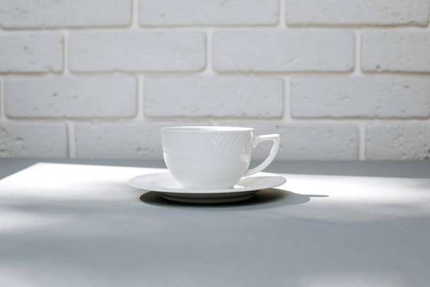 Bílý hrnek s černou kávou na šedém pozadí se stíny listí. Pohled zepředu, zblízka - Fotografie, Obrázek