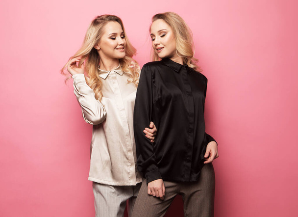Two beautiful young women in casual clothes posing over pink background. Fashion concept. - Foto, immagini