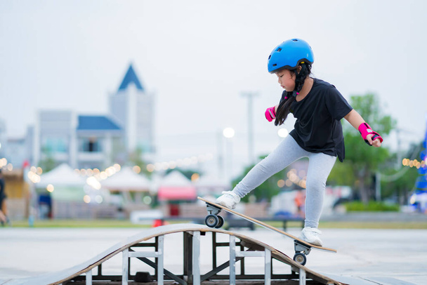 Παιδί ή παιδί κορίτσι που παίζει surfskate ή skateboard στο παγοδρόμιο πατινάζ ή αθλητικό πάρκο στο πάρκινγκ για να φορέσει κράνος ασφαλείας αγκώνα μαξιλάρια καρπό και το γόνατο υποστήριξη - Φωτογραφία, εικόνα