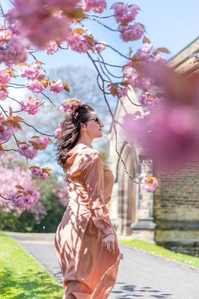 Žena v polovině třicítky v parku s kvetoucími třešněmi nebo sakurou, jaro ve Velké Británii. Užívá si života a slunečného dne s teplým počasím - Fotografie, Obrázek