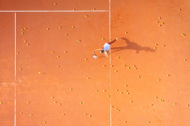 Здоровый образ жизни. Молодая девушка играет в теннис на корте. Вид с воздуха на теннисистку. Грязный суд. Спортивный фон. Вид с воздуха с беспилотника. - Фото, изображение