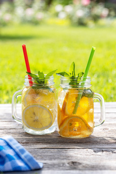 Virkistävä kotitekoinen limonadi tarjoillaan ulkona puutarhapöydässä. Kylmä kesäjuoma tuoreilla sitrushedelmillä ja puutarhamintulla - Valokuva, kuva