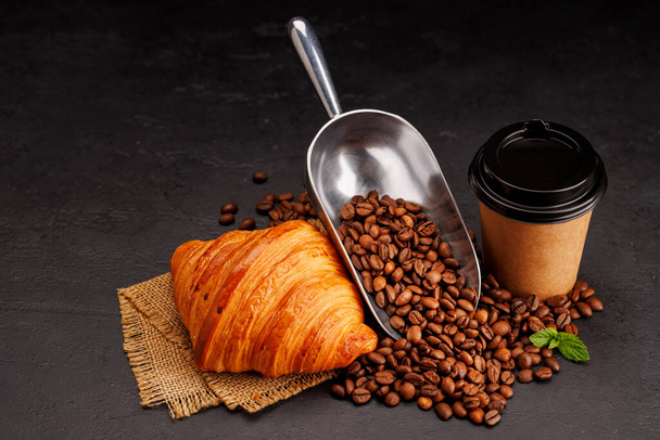 Café aromatique dans une tasse en papier associée à un croissant floconneux et des haricots frais rôtis. Avec espace de copie - Photo, image