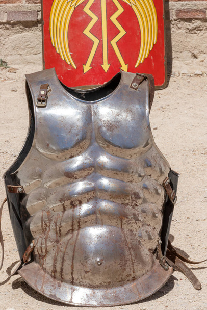 κάθετη άποψη μιας αρχαίας ρωμαϊκής αυτοκρατορίας στρατιώτη πανοπλία cuirass "Lorica Musculata" και κόκκινο χρώμα ορθογώνια ασπίδα "scutum augusta" στο παρασκήνιο  - Φωτογραφία, εικόνα