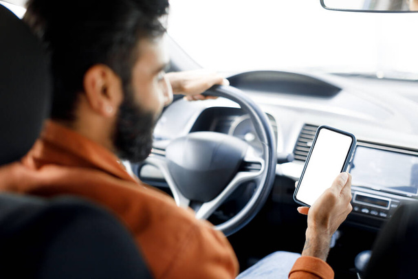Araba Seyrüsefer Başvurusu. Orta Doğulu Sürücü Aracın İçindeki Salonda Boş Ekran ile Akıllı Telefon Kullanıyor, Arka Koltuktan Görüntü. Cep telefonuna Seçici Odaklanma - Fotoğraf, Görsel