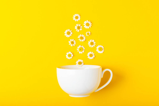 黄色の背景にカモミールの花とカモミール茶のカップ。接近中だ。コピースペース。健康的なハーブドリンク免疫茶。自然療法の概念。テキストのための場所. - 写真・画像