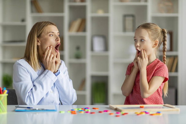 Speech Therapist Woman Making Articulation Exercises With Little Girl At Therapy Session, Cute Preteen Female Child Working On Pronunciation With Logopedist Lady During Meeting In Office - Foto, imagen