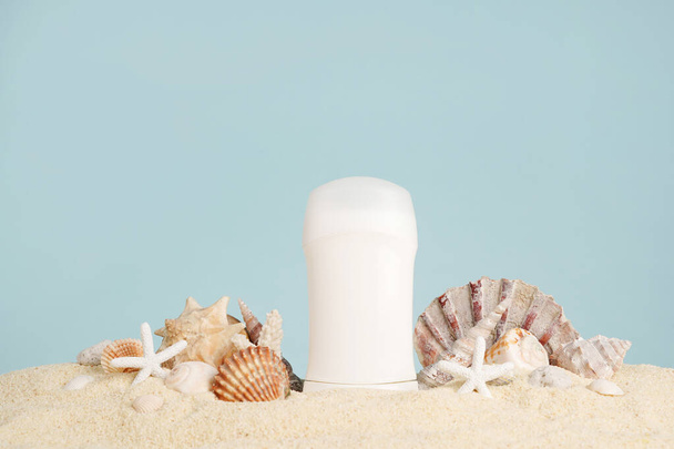 Antitranspirante blanco, desodorante y conchas marinas sobre la arena sobre fondo azul. Concepto de artículos de tocador de minerales marinos y cosméticos orgánicos de verano. Cuidado corporal. Copiar espacio - Foto, imagen