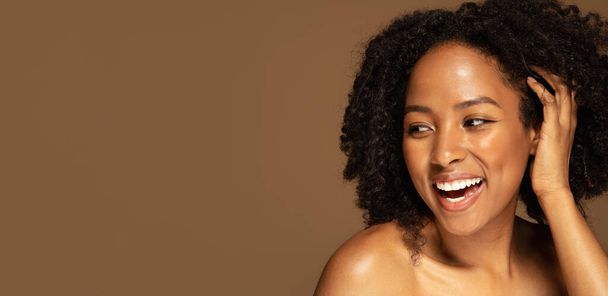 Umarmen Sie Ihre Haut, Akzeptanz, Liebe zum eigenen Körper. Sinnlich schöne halbnackte junge schwarze Frau, die ihr buschiges Haar berührt, lacht und den Kopierraum betrachtet. isoliert auf Studiohintergrund, Web-Banner - Foto, Bild