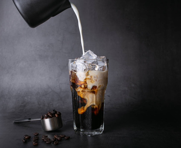 Налийте молоко латеною кавою в прозору склянку з льодом. і смажені кавові зерна на чорному фоні студійне фото
 - Фото, зображення