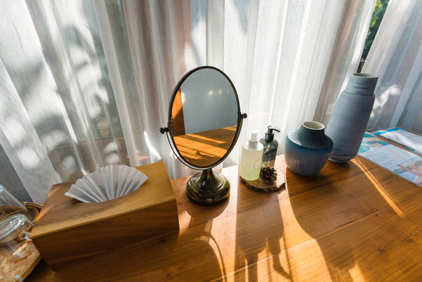 Дерев'яний туалетний столик з дзеркалом, вершками, вазою і тканинною коробкою біля вікна білої завіси в сучасному тропічному курорті
 - Фото, зображення
